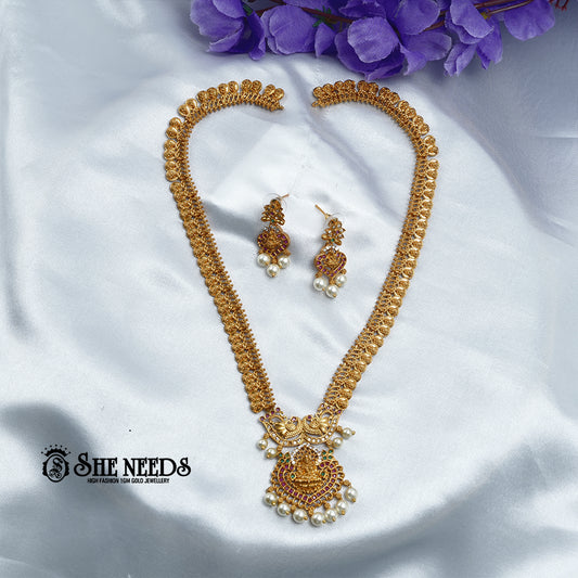 Antique Lakshmi temple coin haram necklace set with ruby stones, pearl drops, Goddess Lakshmi pendant, and matching traditional jhumka earrings on a white fabric background | She Needs Jewellery