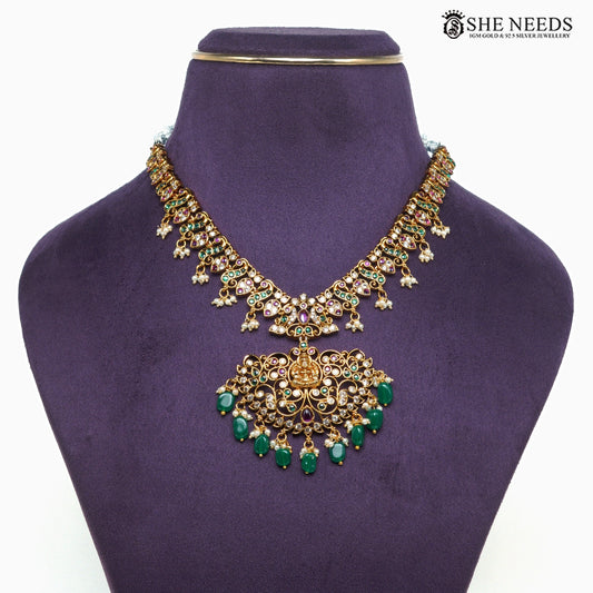 Close-up of gold-plated Lakshmi temple necklace featuring intricate filigree work, green beads, ruby-tone and white stone detailing|She Needs Jewellery