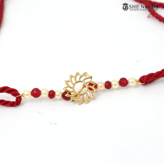 Traditional red and white pearl bead Rakhi with gold floral motif and red braided thread on white background.