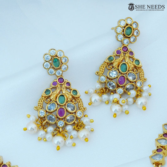 Close-up of Pushpika Gold Plated American Diamond Pearl Jhumka Earrings featuring floral motifs with green and ruby stones, sparkling CZ stones, and elegant pearl drops.|She Needs Jewellery