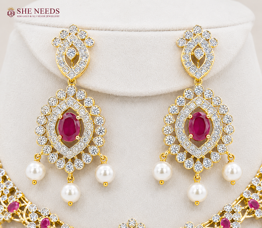 Elegant ruby pink AD stone bridal necklace set with pearl drop earrings in premium gold finish displayed on white mannequin.