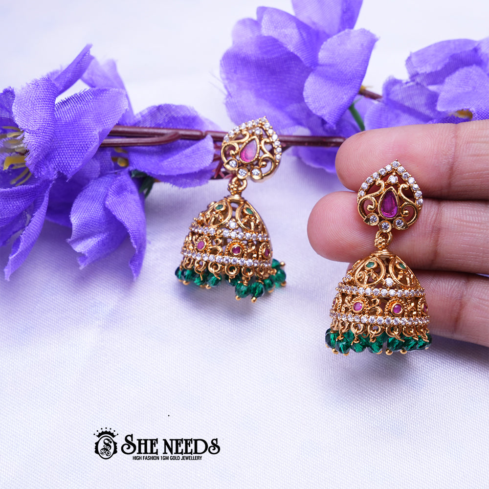Antique gold Aaradhya jhumka earrings featuring sparkling CZ stones, ruby accents, intricate filigree detailing, and emerald green bead drops.|She Needs Jewellery
