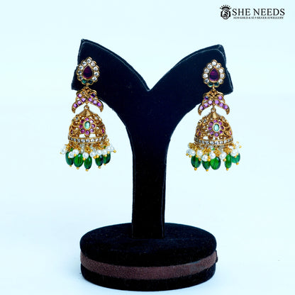 Pair of Aaradhya dome-shaped jhumka earrings with emerald green and ruby pink stones, white pearls, green bead drops and gold polish|She Needs Jewellery