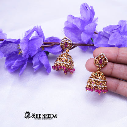 Antique gold Aaradhya jhumka earrings featuring sparkling CZ stones, ruby accents, intricate filigree detailing, and rose pink bead drops.|She Needs Jewellery
