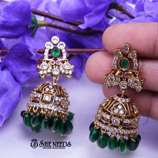 Antique gold jhumka earrings featuring sparkling CZ stones, green center stones, intricate dome detailing, and elegant green bead drops.|She Needs Jewellery
