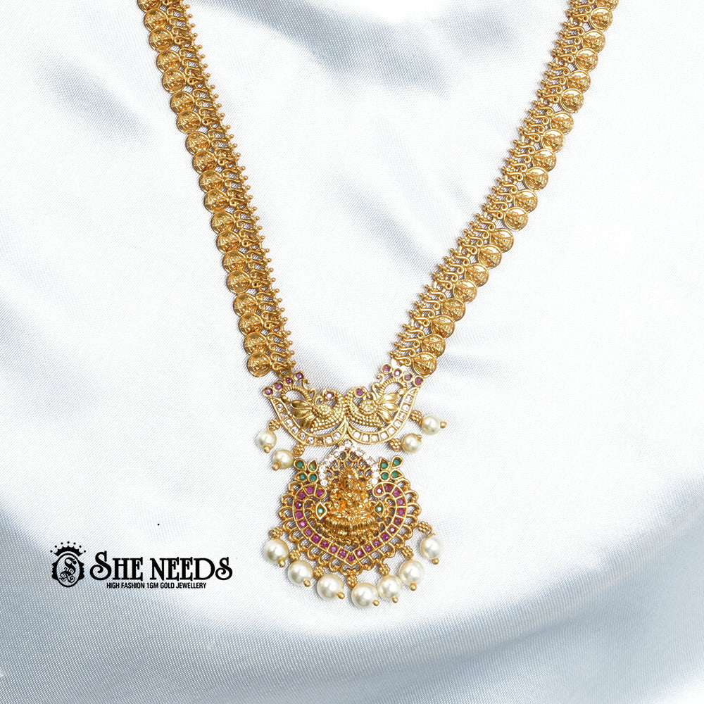 Antique Lakshmi temple coin haram necklace set with ruby stones, pearl drops, Goddess Lakshmi pendant, and matching traditional jhumka earrings on a white fabric background | She Needs Jewellery