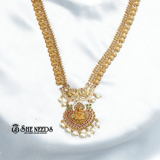Antique Lakshmi temple coin haram necklace set with ruby stones, pearl drops, Goddess Lakshmi pendant, and matching traditional jhumka earrings on a white fabric background | She Needs Jewellery