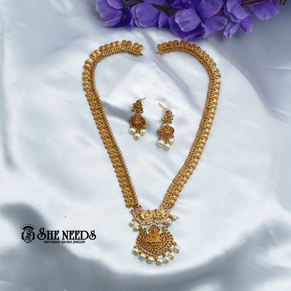 Antique Lakshmi temple coin haram necklace set with ruby stones, pearl drops, Goddess Lakshmi pendant, and matching traditional jhumka earrings on a white fabric background | She Needs Jewellery