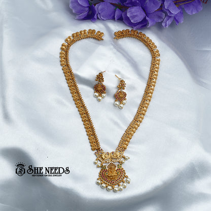Antique Lakshmi temple coin haram necklace set with ruby stones, pearl drops, Goddess Lakshmi pendant, and matching traditional jhumka earrings on a white fabric background | She Needs Jewellery