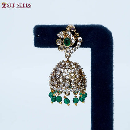 Bloomstone Green AD Jhumka Earrings featuring sparkling American Diamonds, antique gold detailing, green center stone, and matching green crystal drops.|She Needs Jewellery