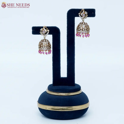 Bloomstone Light Pink AD Jhumka Earrings featuring sparkling American Diamonds, antique gold detailing, light pink center stone, and matching light pink crystal drops.|She Needs Jewellery
