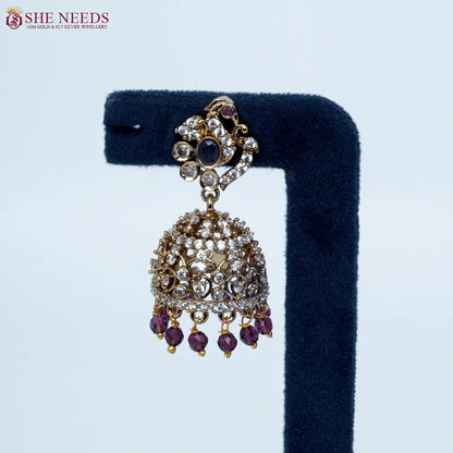 Bloomstone Purple AD Jhumka Earrings featuring sparkling American Diamonds, antique gold detailing, purple center stone, and matching purple crystal drops.|She Needs Jewellery