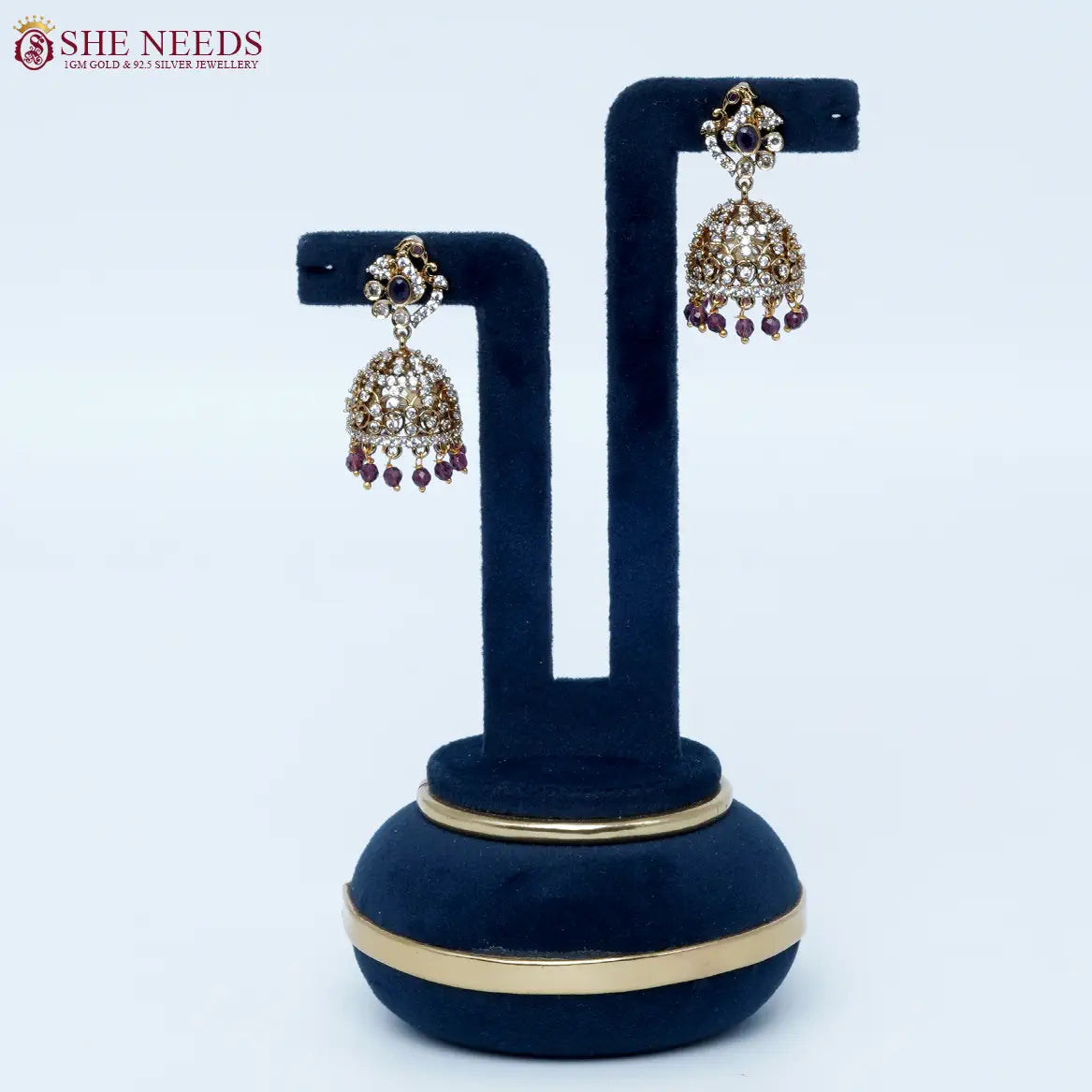 Bloomstone Purple AD Jhumka Earrings featuring sparkling American Diamonds, antique gold detailing, purple center stone, and matching purple crystal drops.|She Needs Jewellery
