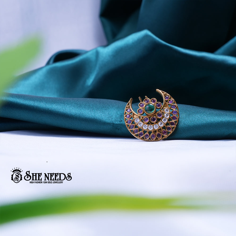 Antique gold crescent-shaped saree pin featuring sparkling kundan stones, ruby-pink accents, and an emerald-green center stone with celestial-inspired detailing.|She Needs Jewellery
