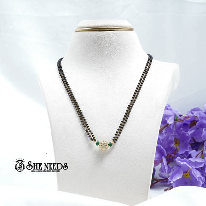 Emerald green dual-string mangalsutra with black beads, CZ-studded spherical pendant, green bead accents, and gold-tone finish displayed on a white jewelry bust |She Needs Jewellery
