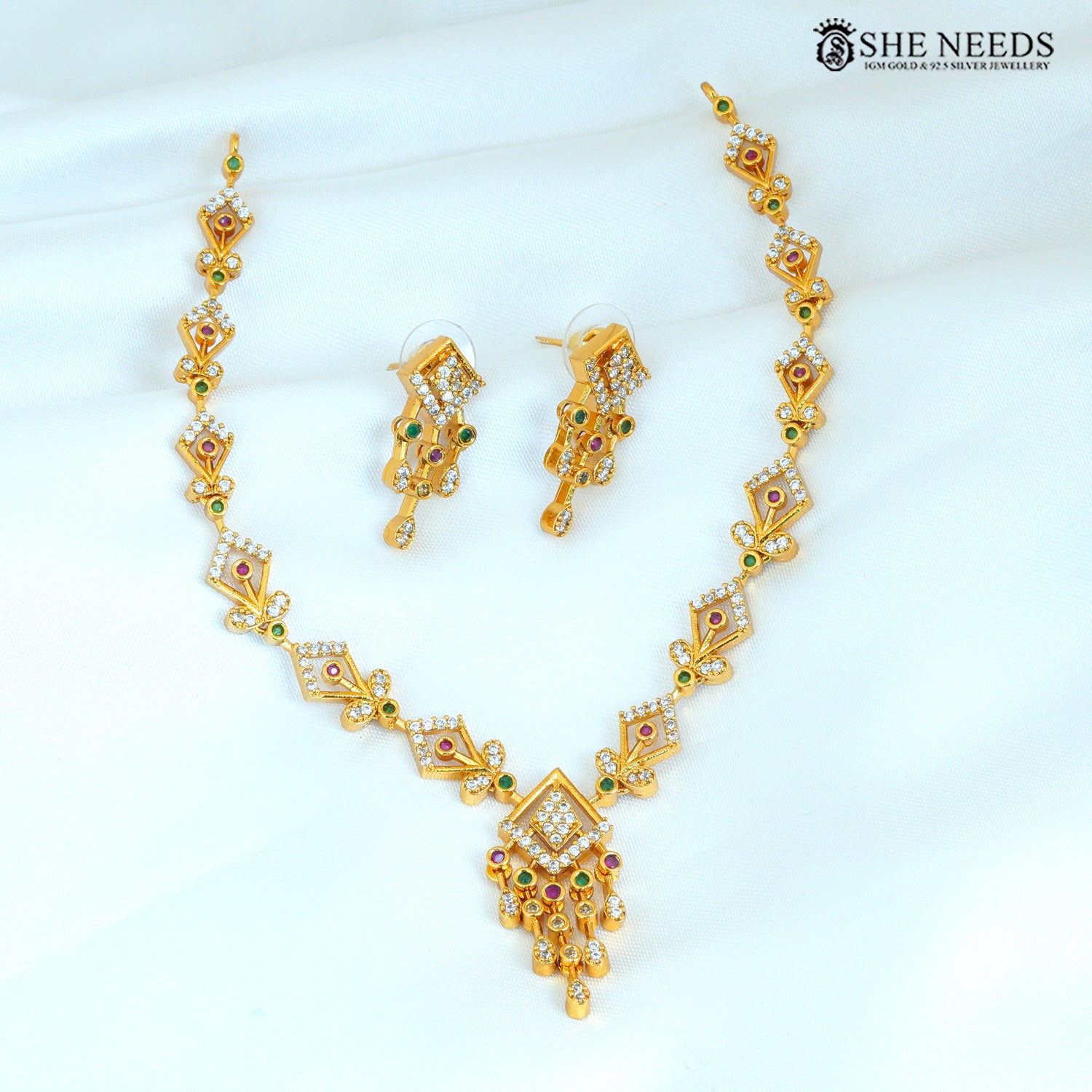 Geometric gold necklace set with matching earrings featuring ruby, green and white stones and a statement pendant
|She Needs Jewellery