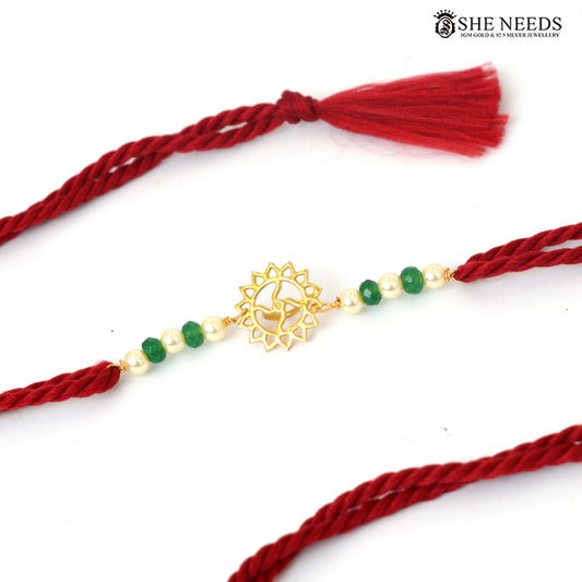 Close-up of gold-plated floral Rakhi with green beads, pearl accents and red thread|She Needs Jewellery
