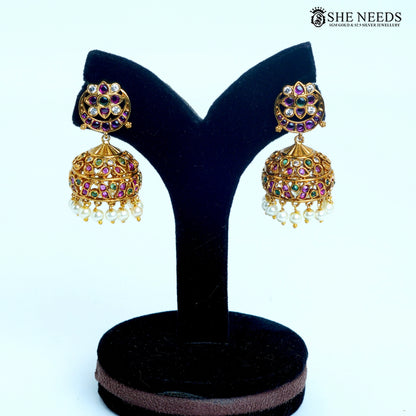 Pair of Ishani floral dome jhumka earrings featuring pink and green stones, white sparkling details and pearl drops on a black jewellery stand|She Needs Jewellery
