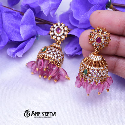 Antique gold Kavya jhumka earrings featuring sparkling CZ stones, ruby center accents, green stone details, and pink bead drops.|She Needs Jewellery
