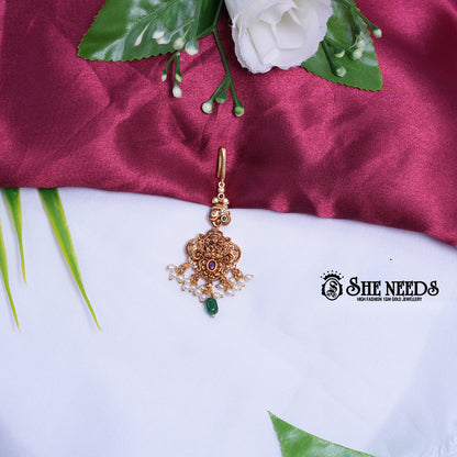 Lakshmi Motif Pearl Maang Tikka in antique gold finish featuring pearl bunches, sparkling stones, and an emerald green stone drop. | she needs jewelry