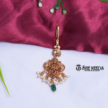 Lakshmi Motif Pearl Maang Tikka in antique gold finish featuring pearl bunches, sparkling stones, and an emerald green stone drop. | she needs jewelry