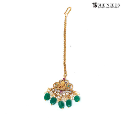 Gold-plated Lakshmi temple maang tikka with green bead drops, white stones, ruby-tone accents and pearl detailing|She Needs Jewellery
