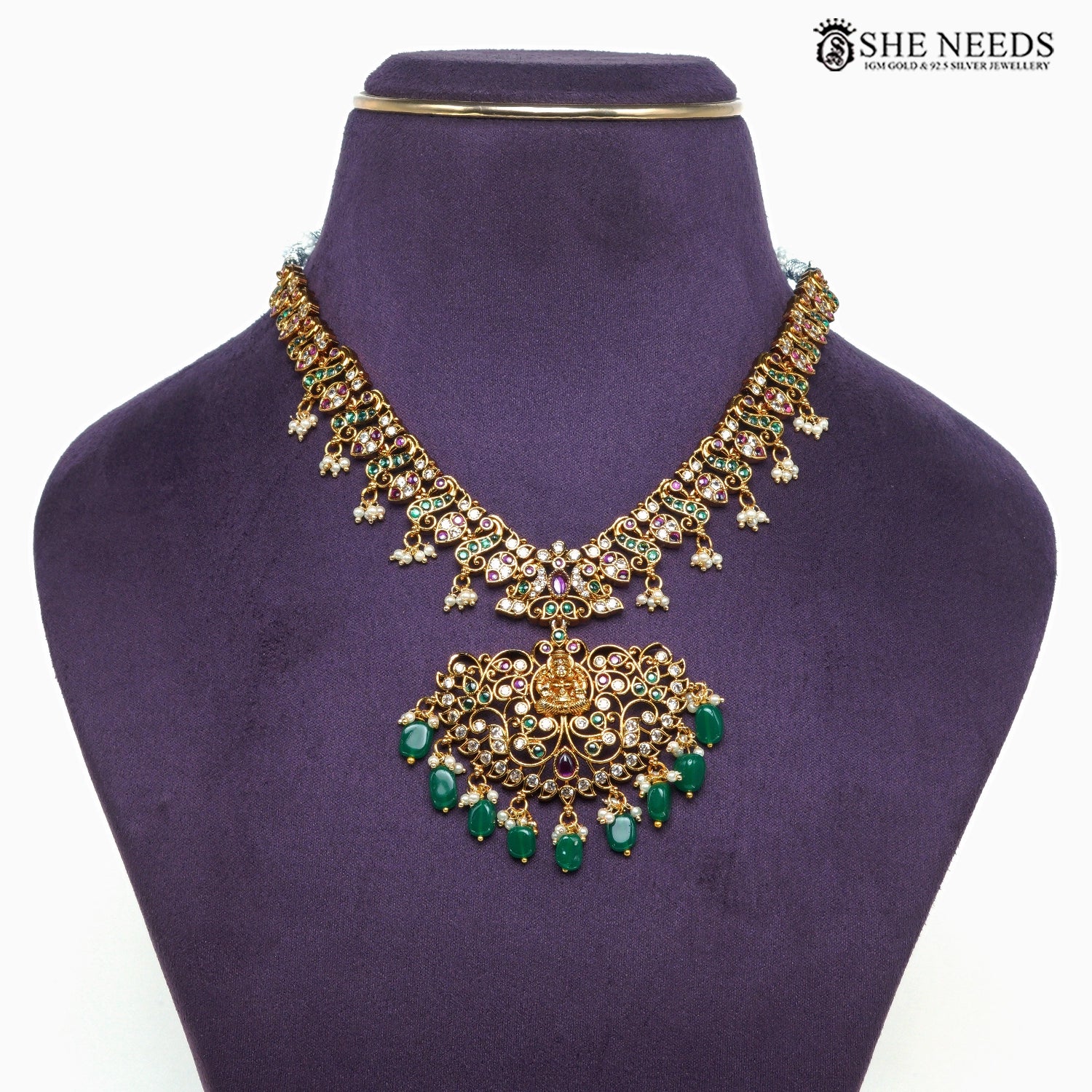 Close-up of gold-plated Lakshmi temple necklace featuring intricate filigree work, green beads, ruby-tone and white stone detailing|She Needs Jewellery
