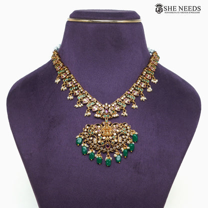 Close-up of gold-plated Lakshmi temple necklace featuring intricate filigree work, green beads, ruby-tone and white stone detailing|She Needs Jewellery

