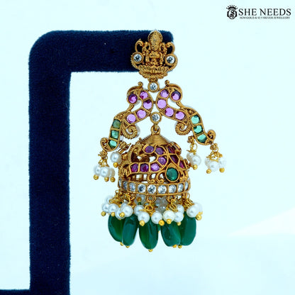 Close-up of Lakshmika Antique Gold Temple Jhumka Earring showcasing a Lakshmi deity motif, ruby-colored stones, American Diamonds, pearl accents, and green bead drops.|She Needs Jewellery
