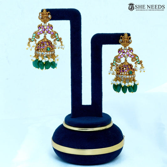 Pair of Lakshmika Antique Gold Temple Jhumka Earrings featuring a Lakshmi deity motif, ruby-colored stones, American Diamonds, pearl accents, and green bead drops.|She Needs Jewellery
