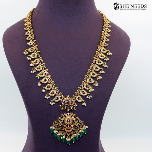 Gold-plated peacock-inspired necklace with intricate stonework, green accents, ruby-toned stones and pearl drops displayed on a jewellery bust|She Needs Jewellery