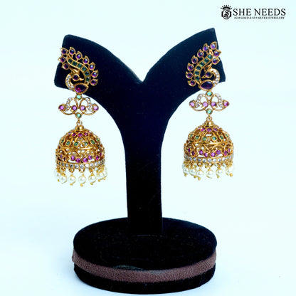 Mayura Royale peacock curve jhumka earring featuring pink and green stones, white detailing and pearl drops in gold-tone finish|She Needs Jewellery
