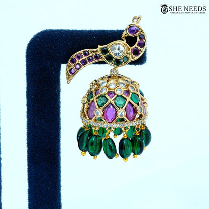 Close-up of Mayurika Antique Gold Peacock Feather Jhumka Earring featuring ruby-colored stones, American Diamonds and green bead drops.|She Needs Jewellery
