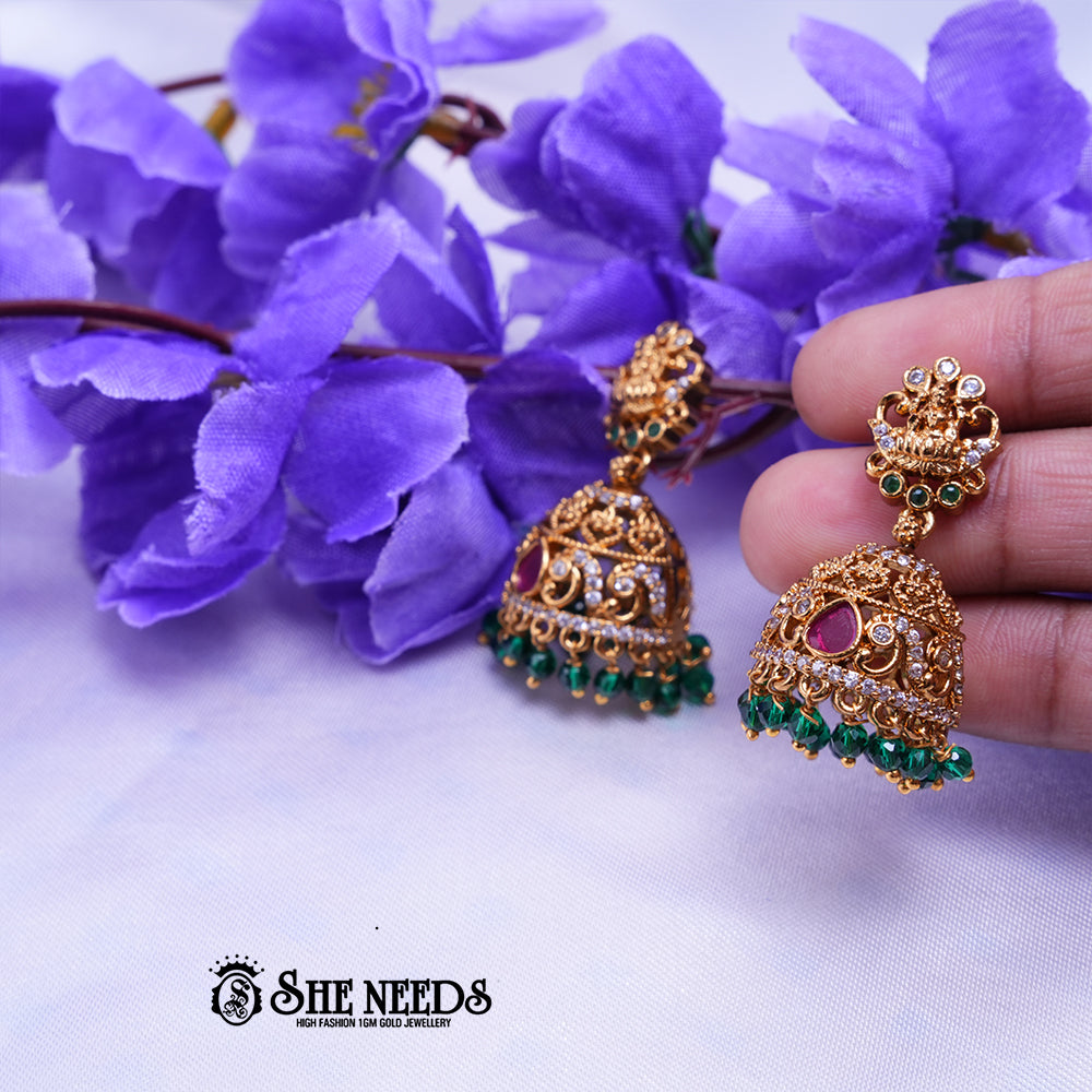 Antique gold Meher temple jhumka earrings featuring CZ stones, ruby-pink stone accents, temple-inspired stud detailing, and green bead drops.|She Needs Jewellery
