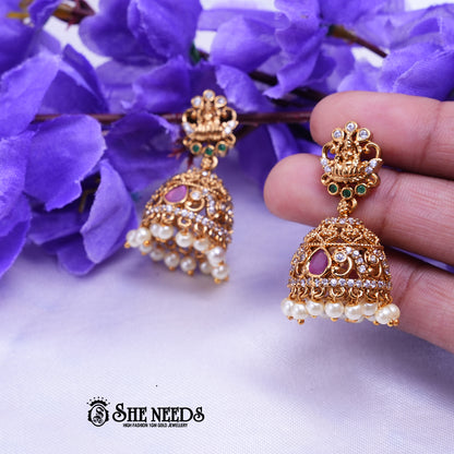 Antique gold Meher temple jhumka earrings featuring CZ stones, ruby-pink stone accents, temple-inspired stud detailing, and pearl drop danglers.|She Needs Jewellery
