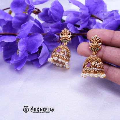 Antique gold Meher temple jhumka earrings featuring CZ stones, ruby-pink stone accents, temple-inspired stud detailing, and pearl drop danglers.|She Needs Jewellery
