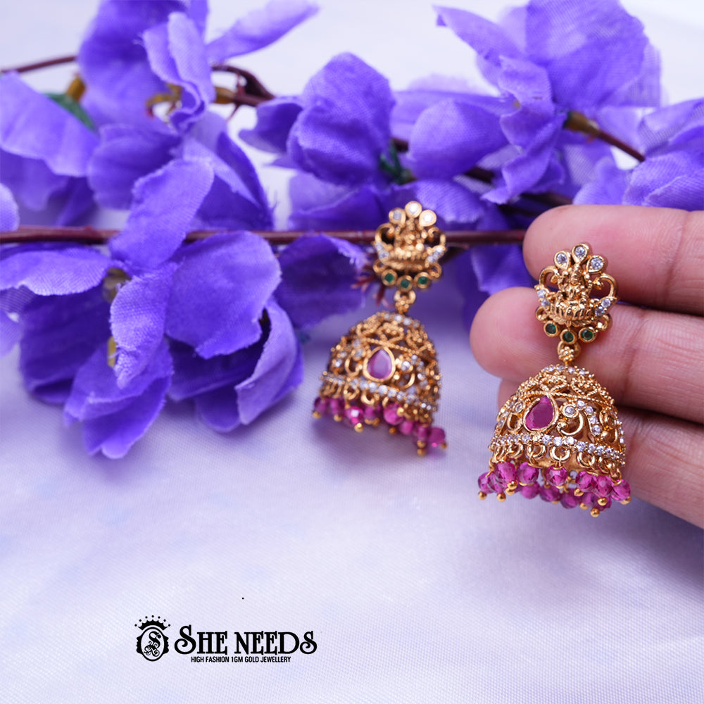 Antique gold Meher temple jhumka earrings featuring CZ stones, ruby-pink stone accents, temple-inspired stud detailing, and pink bead drops.|She Needs Jewellery
