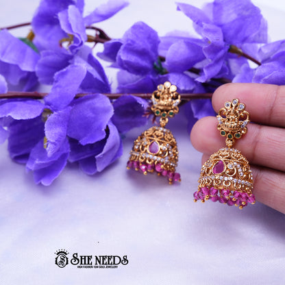 Antique gold Meher temple jhumka earrings featuring CZ stones, ruby-pink stone accents, temple-inspired stud detailing, and pink bead drops.|She Needs Jewellery
