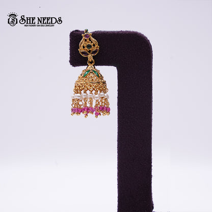 Antique gold Nakshi Pearl Cascade Jhumkas featuring emerald-green and pink stones, layered pearl danglers, pink bead drops, and intricate temple-style craftsmanship displayed on a velvet stand.|She Needs Jewellery
