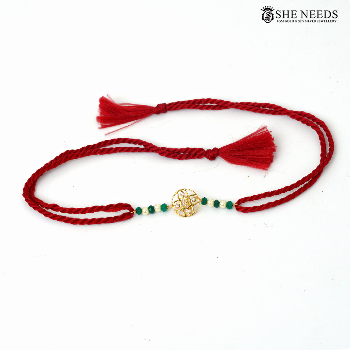 Traditional green bead Rakhi with gold-tone decorative motif and red braided thread on white background.