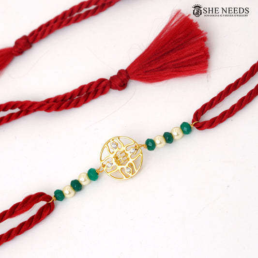 Traditional green bead Rakhi with gold-tone decorative motif and red braided thread on white background.