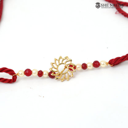 Traditional red and white pearl bead Rakhi with gold floral motif and red braided thread on white background.