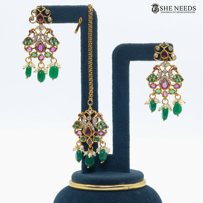 Pair of gold-plated peacock-inspired earrings with green bead drops, ruby-toned stones, white stones and pearl accents|She Needs Jewellery