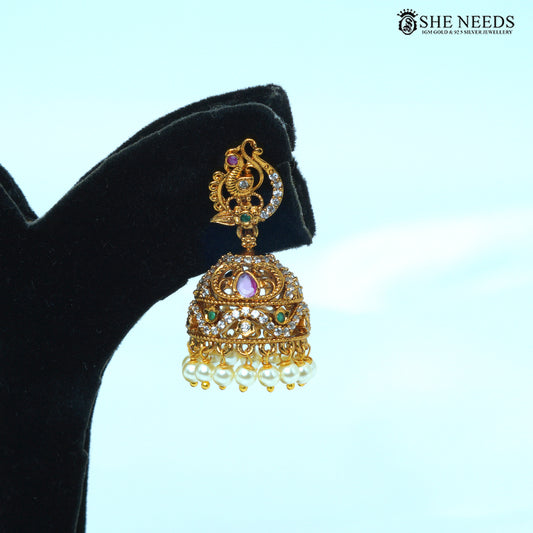 Close-up of a peacock motif jhumka earring with green and pink stones, white stones and pearl drops