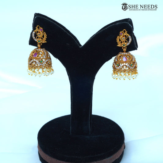 Pair of peacock motif jhumka earrings with green and pink stones, intricate gold detailing and white pearl drops|She Needs Jewellery
