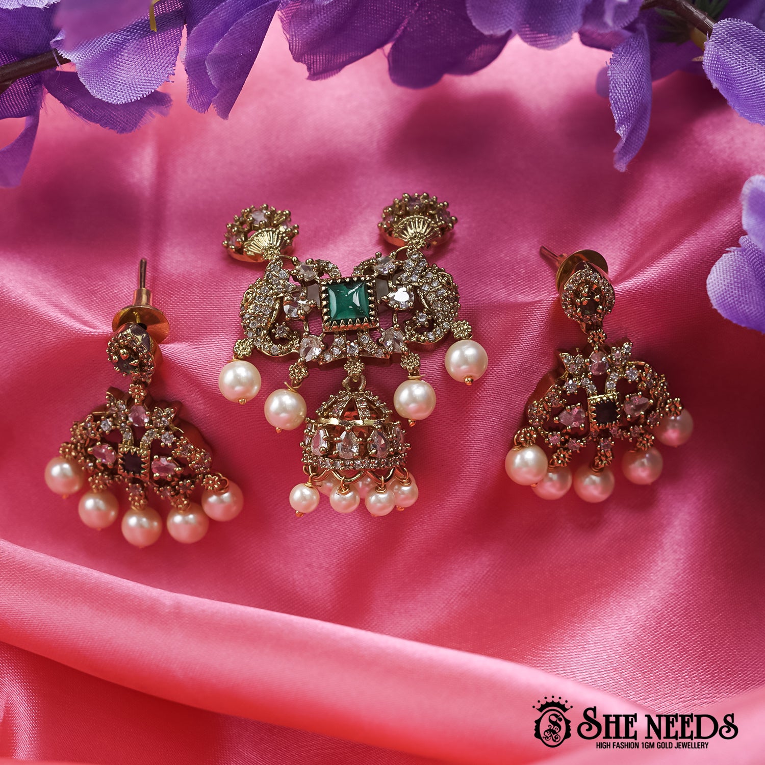 Regal Emerald Pearl Jhumka Set featuring an emerald green center stone, sparkling American Diamonds, pink stone accents, matching earrings, and elegant pearl drops in an antique gold finish.|She Needs Jewellery
