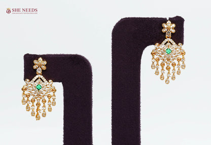 Gold-plated chandelier earrings with American diamonds, emerald green center stone, floral stud, and elegant tassel drops for bridal and festive wear.|She Needs Jewellery
