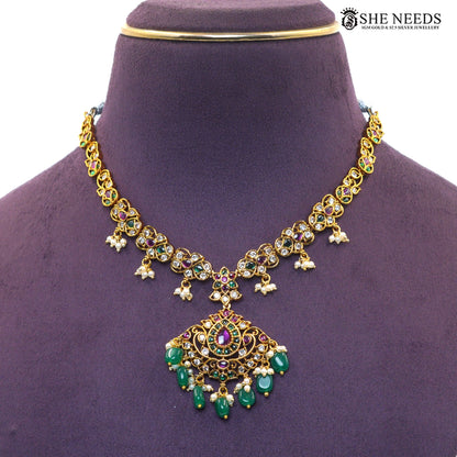 Close-up of royal emerald necklace pendant featuring a teardrop ruby-style centerpiece, green stones, white stones and pearl drops|She Needs Jewellery
