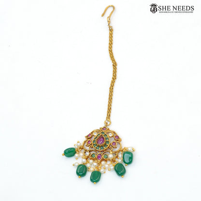Traditional gold-toned maang tikka featuring green emerald-style stones, ruby accents, pearl drops and intricate temple-inspired detailing|She Needs Jewellery
