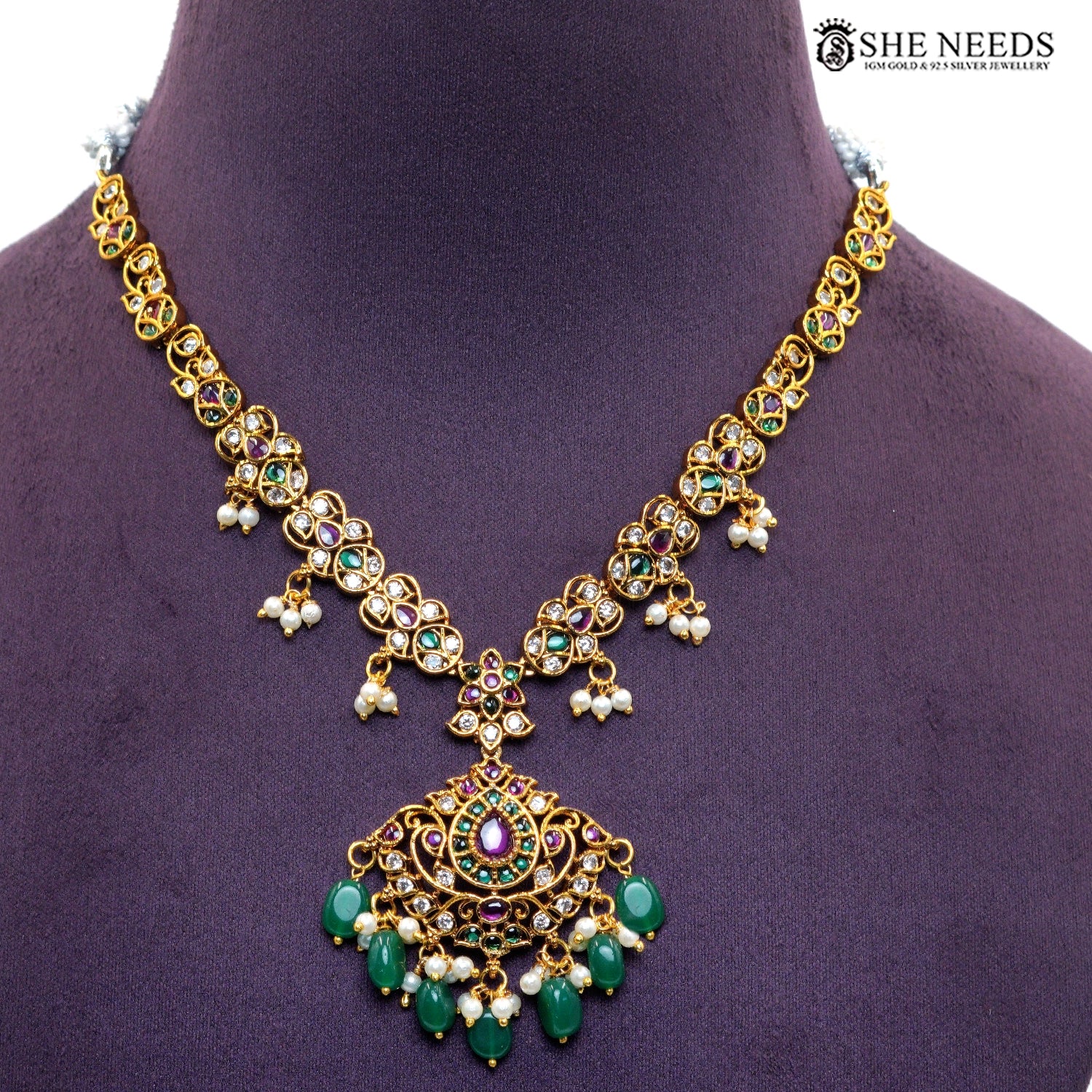 Close-up of ornate royal necklace pendant with green emerald-style stones, ruby accents, white stones and multiple pearl and green bead drops|She Needs Jewellery
